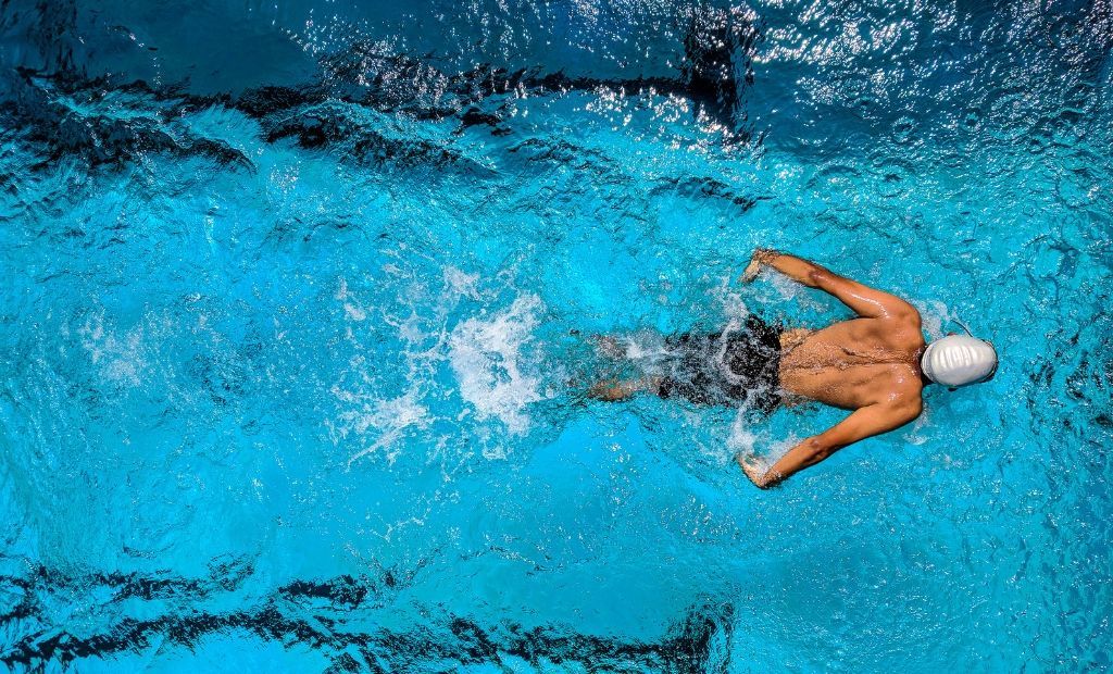 A male swimmer wearing a swimming cap practising front crawl in a swimming pool 